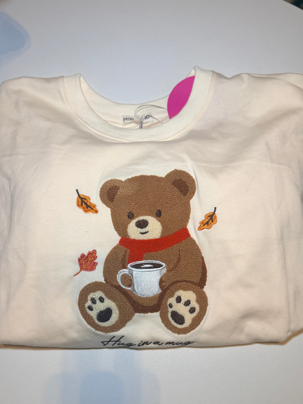 Folded cream Hug in a Mug sweatshirt with teddy bear and autumn leaves