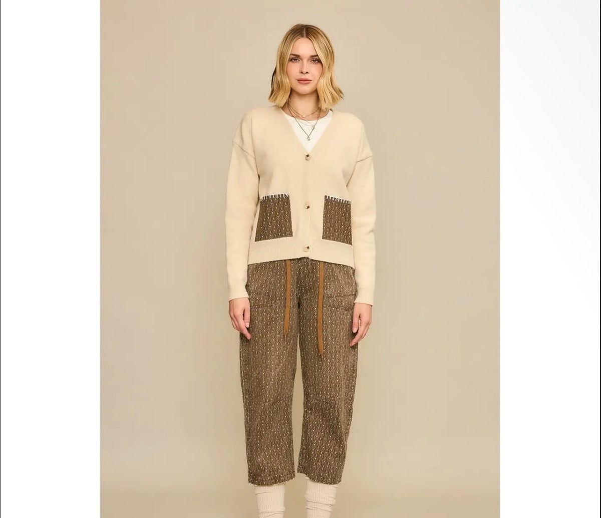 Model wearing a natural knit cardigan with brown geometric-print contrast pockets and matching cropped barrel-leg pants.